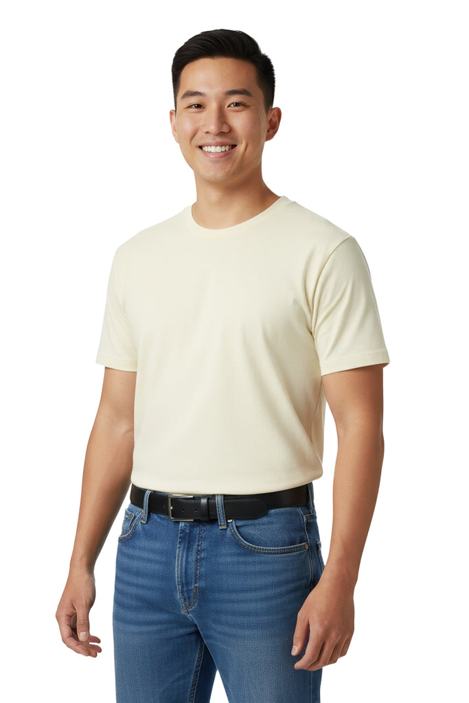 Smiling man with short dark hair stands against a dark background, wearing a cream t-shirt, blue jeans, and a black belt.