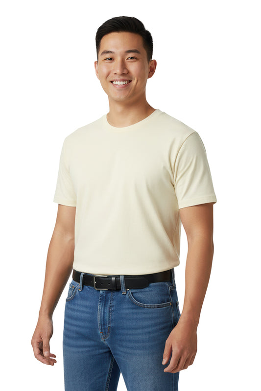 Smiling man with short dark hair stands against a dark background, wearing a cream t-shirt, blue jeans, and a black belt.