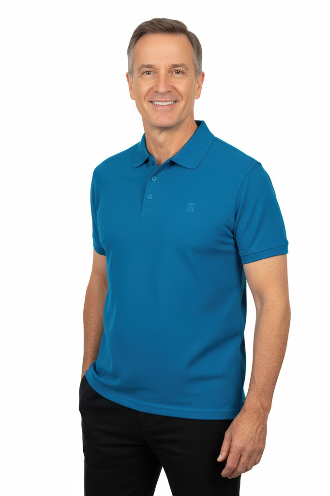 Smiling man with short graying hair wears a blue polo shirt with a subtle logo on the chest and black pants, with his hand in a pocket.