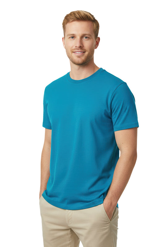 Smiling blonde man with a beard stands with his hands in the pockets of his tan pants, wearing a bright blue t-shirt.