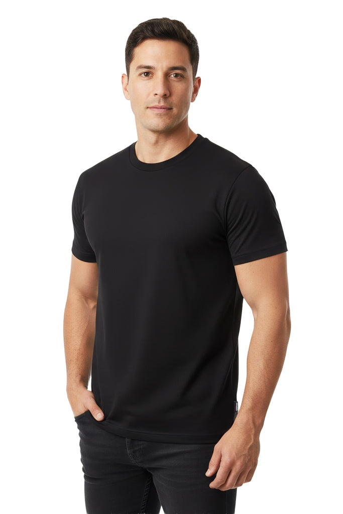 Man with short dark hair wears a plain black crew neck t-shirt and black jeans, standing with one hand in his pocket.