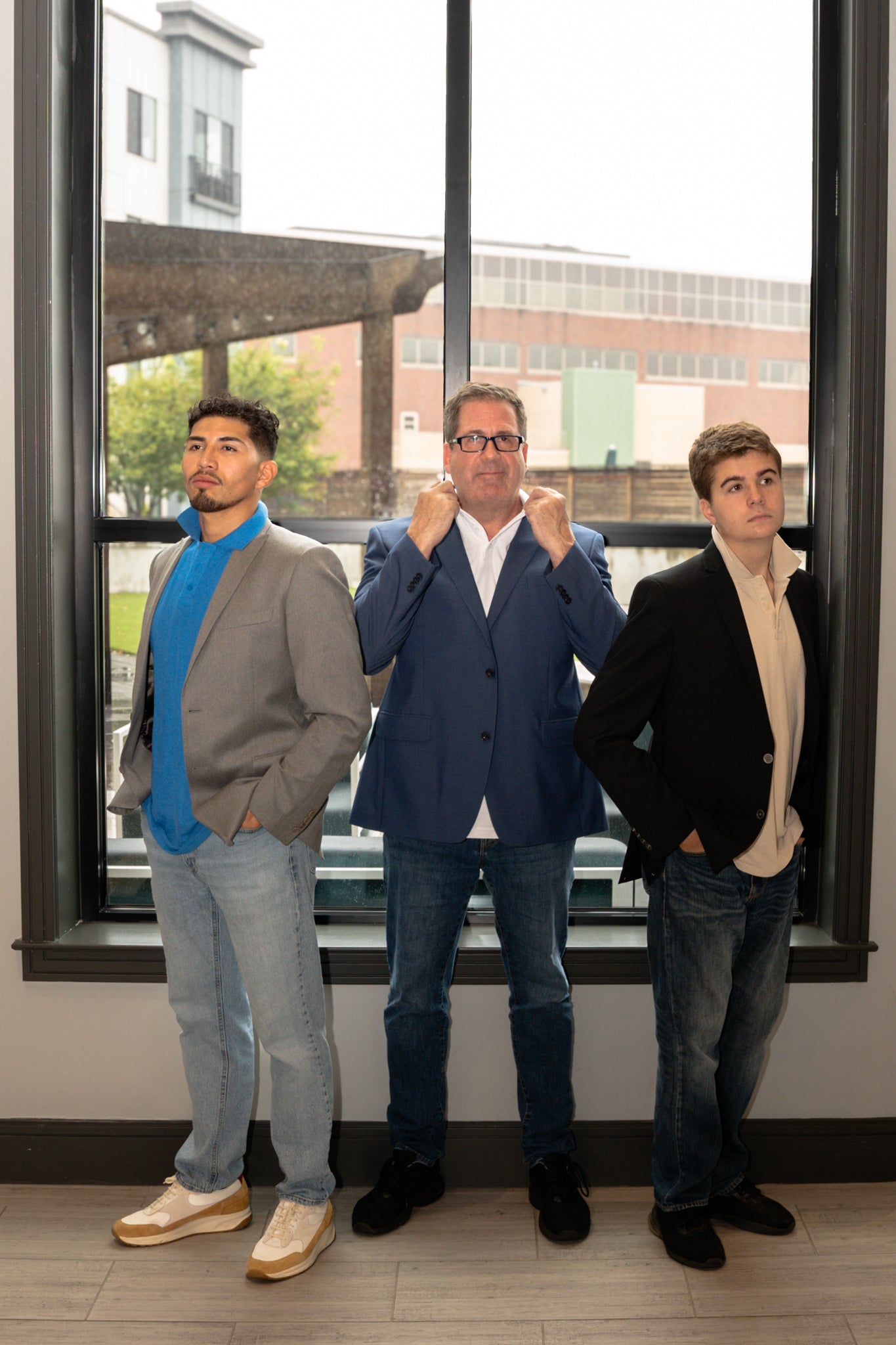 three men standing and posing in front of a window