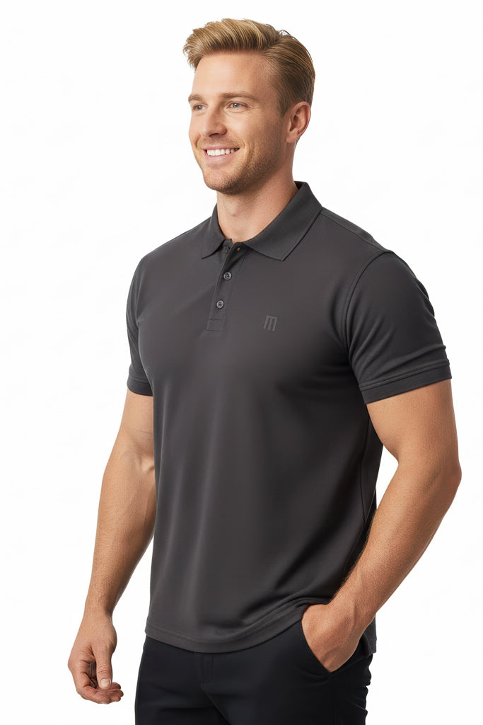 smiling man with short light hair wearing a dark gray polo shirt and black pants, with one hand in his pocket.