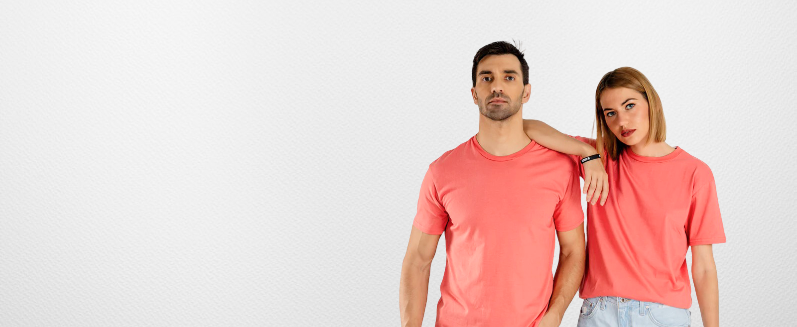 Man and a woman posing together, both wearing plain coral-colored t-shirts against a white background. The woman is resting her hand on the man's shoulder.